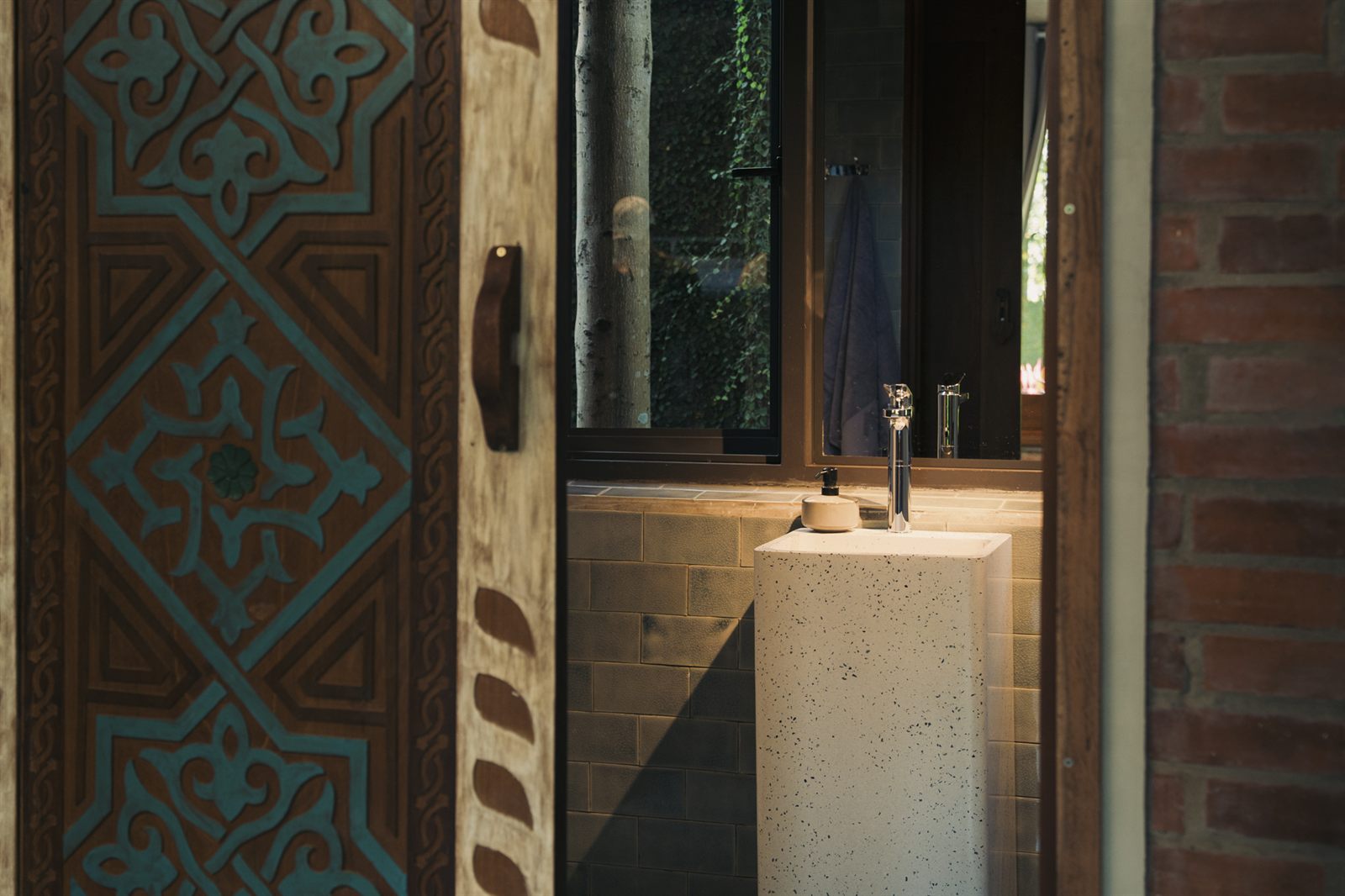 Carved wooden door beside a stone basin, with a window onto the garden