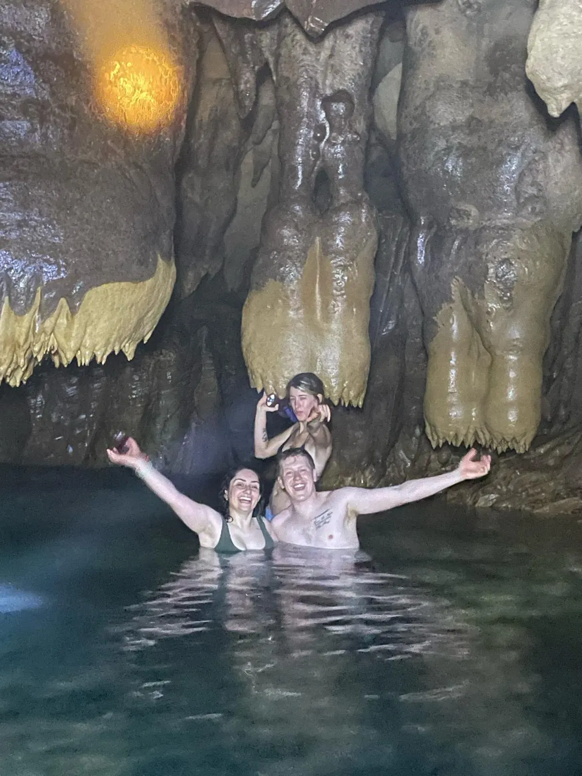 Three riders swimming in a cave pool under the stalactites, arms up