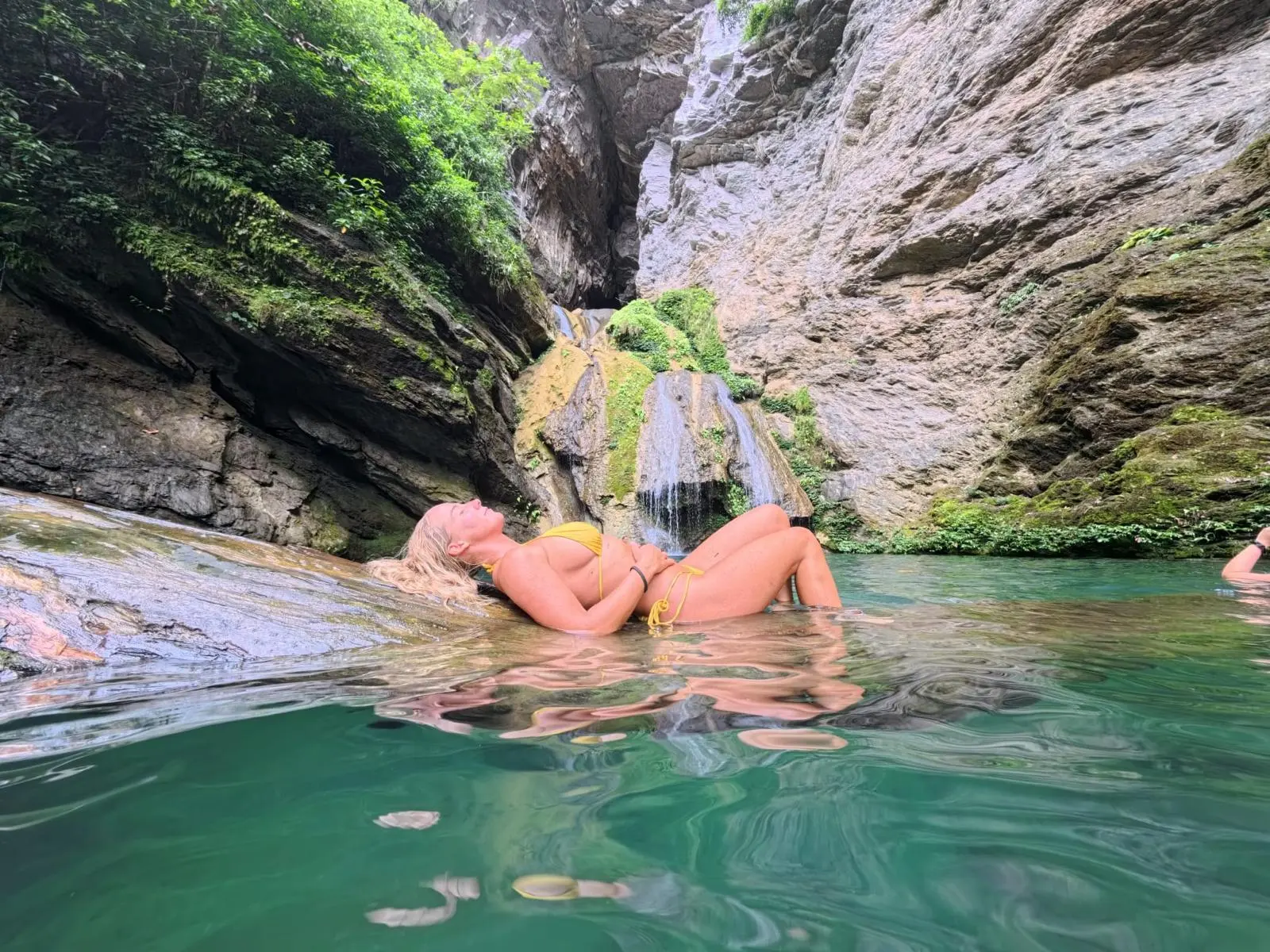 A guest lying back on the rock at the edge of a green waterfall pool